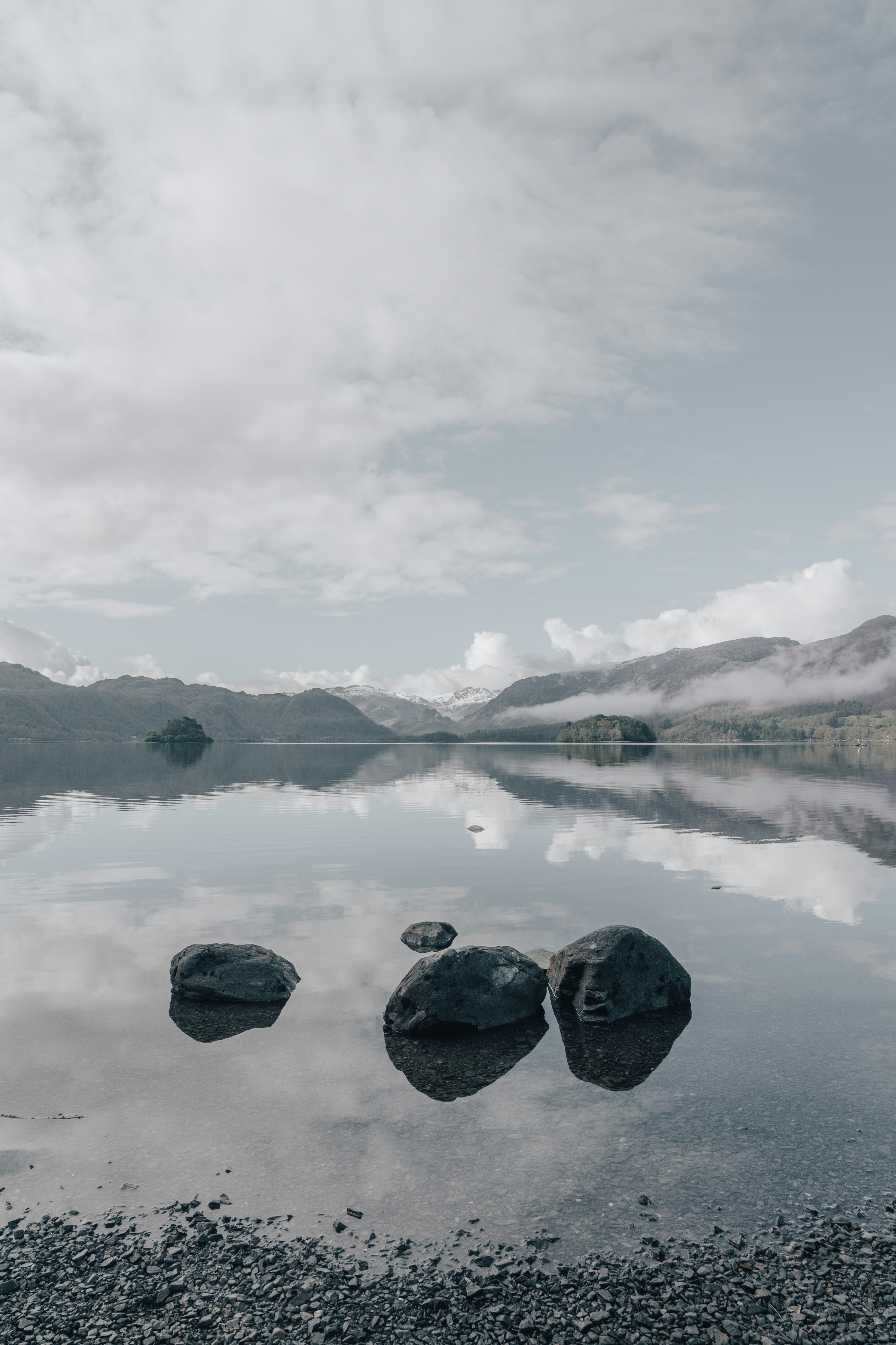 body of water near mountain under white sky during daytime